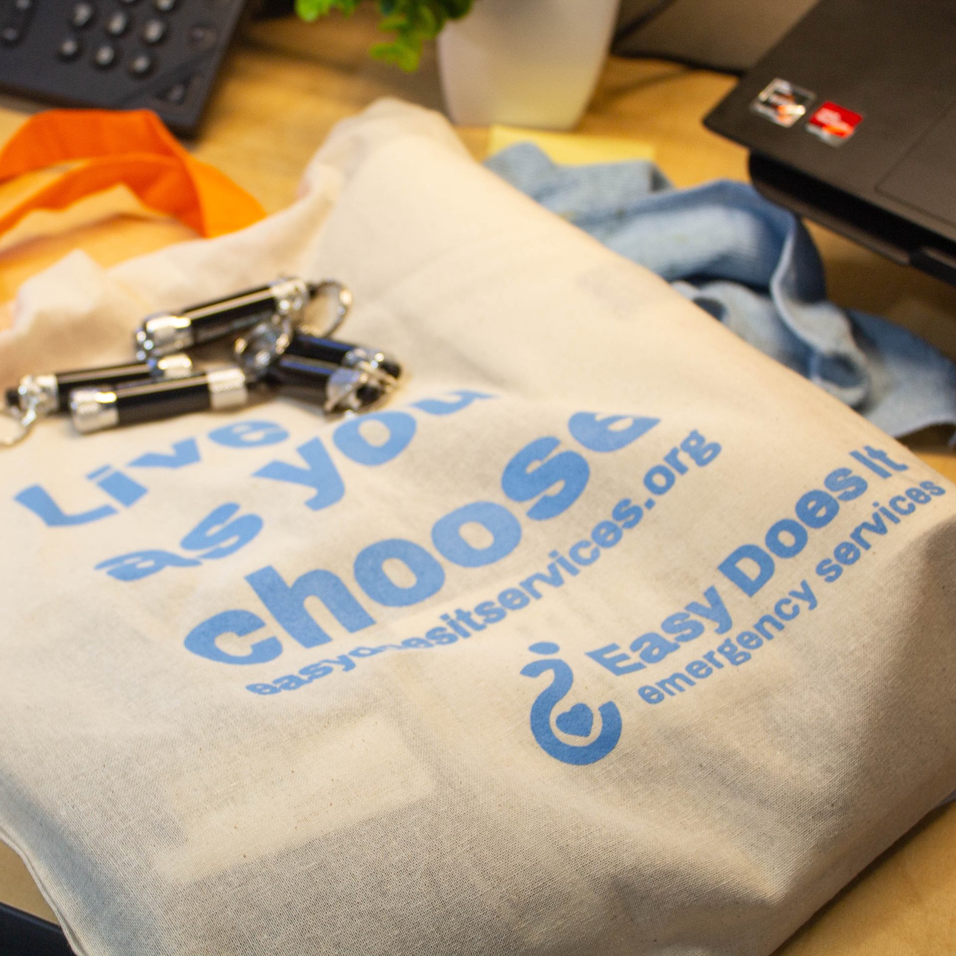 A photo of Easy Does It's Summer 2024 Tote Bag. With an updated color palette and plastic-free materials. As well as our brand new Easy Does It Flashlights.